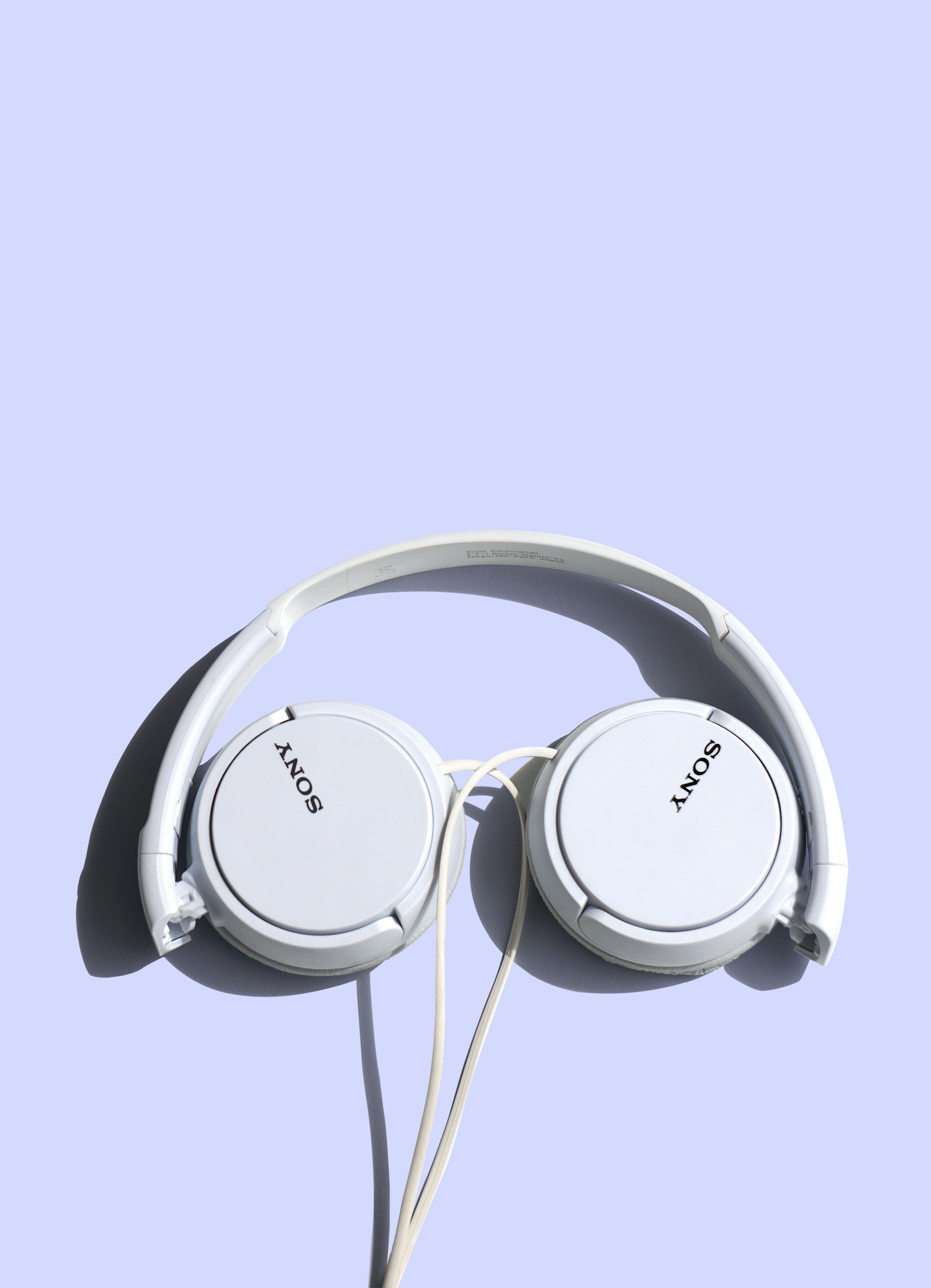 White Sony on-ear headphones with a slim headband on a pale blue background.
